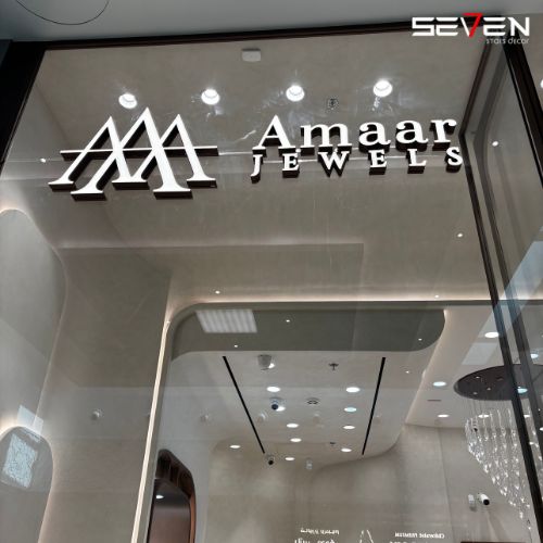 The sleek, modern entrance of 'Amaar Jewels' store designed by Seven Star, featuring illuminated signage on glass and a glimpse of a luxurious interior, showcasing commercial fit-out specialists in UAE expertise.
