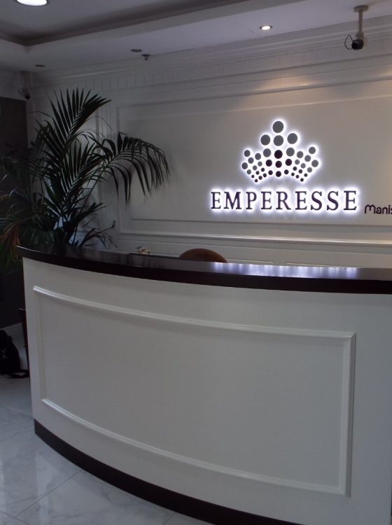 A luxurious and elegant reception area for 'EMPERESSE manish JEWELLERS GROUP CO.' designed by Seven Star, featuring a curved wooden desk, classic wall molding, and illuminated branding, showcasing luxury interior design firm in UAE expertise.