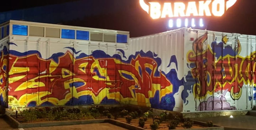 The vibrant exterior of Barako Grill at night, designed by Seven Star in Dubai, featuring shipping containers covered in colorful graffiti and an illuminated bull-horn sign, showcasing their expertise as commercial fit-out specialists in UAE.